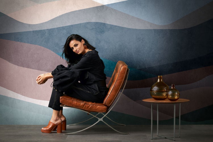 Frau sitzt auf einem Barcelona-Sessel vor einer Wandtapete mit Wellenmuster
