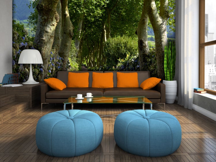 Wohnzimmer mit braunem Sofa, Poufs und Baumallee-Fototapete für ein helles Ambiente