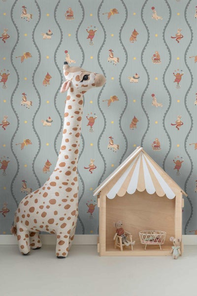 Kindertapete mit Zirkusmotiven und gewellten Linien in einem Kinderzimmer mit einer großen Plüschgiraffe und einem Spielhaus aus Holz.