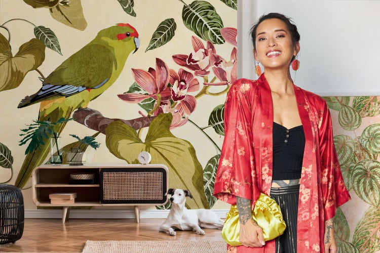 Dekoratives Wohnzimmer mit einer Frau, einem Hund, einer Kommode und einer tropischen Tapete mit einem Papagei und floralen Motiven.