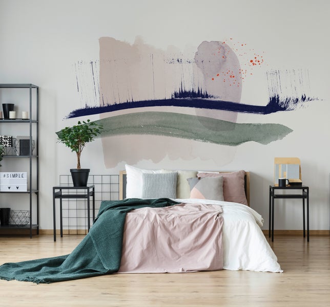 Helles, modernes Schlafzimmer mit großflächiger abstrakter Fototapete im Aquarell-Stil, Bett mit Textilien, schwarzen Beistelltischen und Regal.