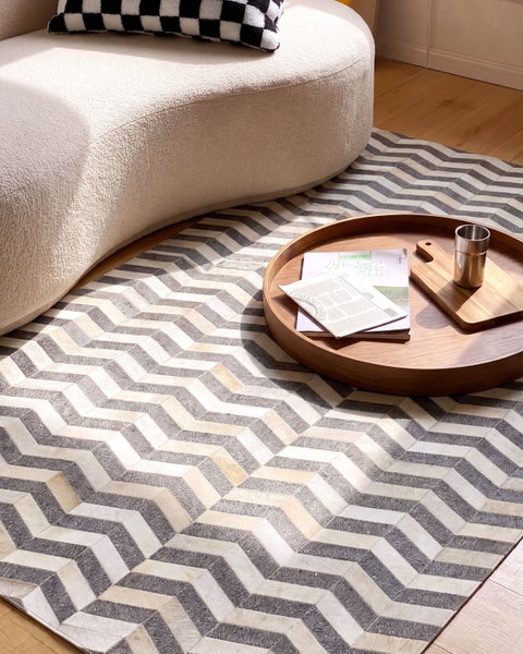 Teppich mit Zickzackmuster auf Holzboden neben einem Sofa mit geschwungener Form und einem runden Holztablett mit Dekoration.