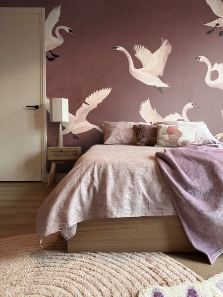 Schlafzimmer mit Bett, Nachttisch, Lampe und Tapete mit Schwanenmotiven.