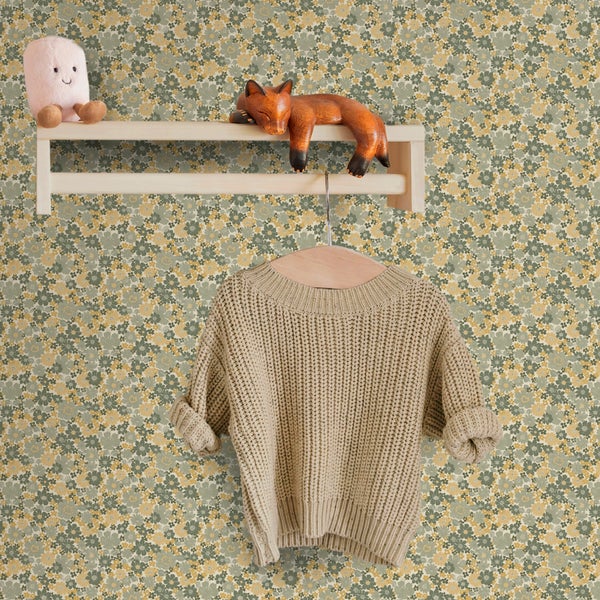 Vliestapete mit feinem Blumenmuster an einer Wand mit Holzregal und aufgehängtem Strickpullover im Kinderzimmer-Stil.