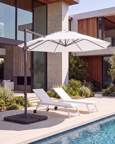 Moderner Außenbereich mit weißem Ampelschirm, zwei Sonnenliegen am Pool und zeitgenössischem Haus aus Beton und Glas.
