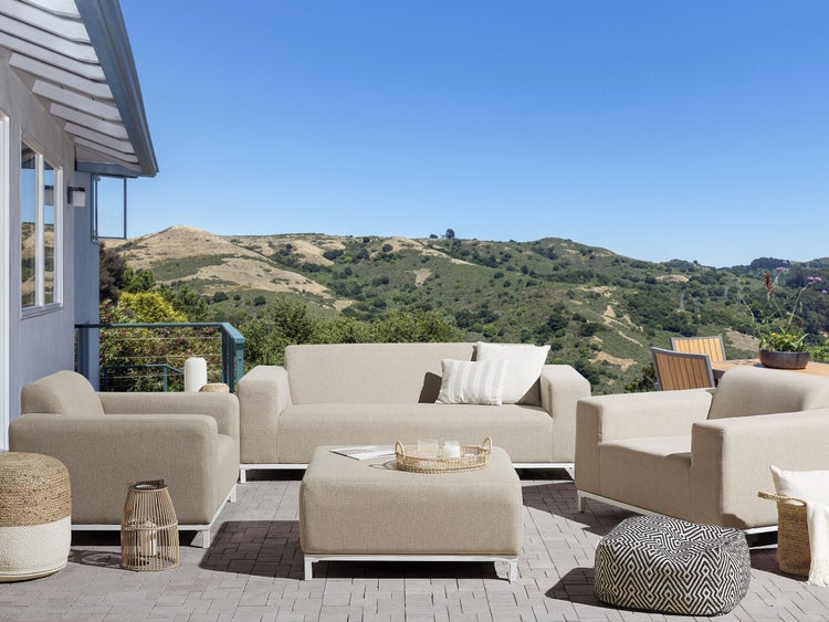 Terrasse mit Sofa, Sesseln, Hocker und Beistelltischen vor einer Hügellandschaft.