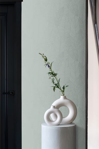 Raumansicht mit Blattmuster-Tapete, Dekoration mit Vasen und einem Blumenarrangement.