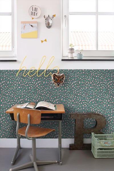 Verspieltes Kinderzimmer mit Leopardenmuster-Tapete in Türkis und Rosa, Holzschreibtisch, großem Buchstaben R und hellen Fenstern.