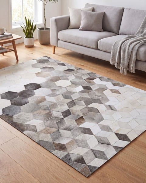 Wohnzimmer mit einem rechteckigen Teppich aus geometrischen Mustern vor einem hellen Sofa auf einem Holzboden.