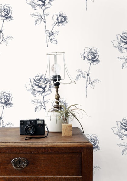 Dekorative Tapete mit Rosenmuster in einem Raum mit einem Nachttisch, einer Lampe und einer Kamera.