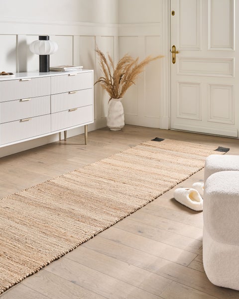 Langer gewebter Juteläufer auf Holzfußboden in einem hellen, organisierten Zimmer mit weißem Sideboard und Vase.