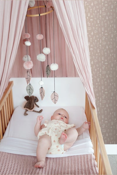 Baby liegt in einem Kinderbett mit Mobile und Baldachin