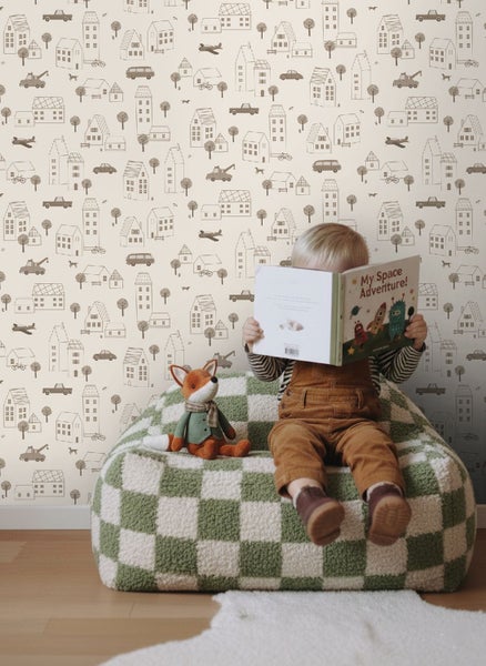 Kind liest Buch auf einem Schachbrett-Sitzsack vor einer Tapete mit Stadtmotiven