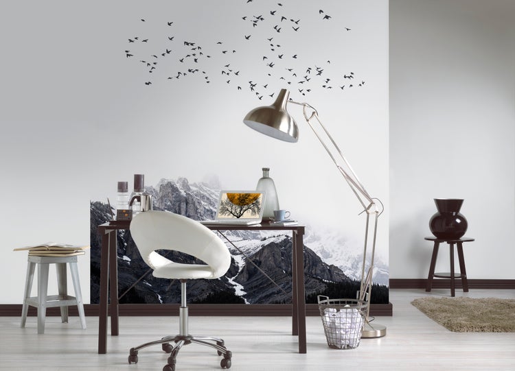 Fototapete mit Bergpanorama und Vogelschwarm in einem modern eingerichteten Büro mit dunklem Schreibtisch, weißem Bürostuhl und Metall-Stehlampe.