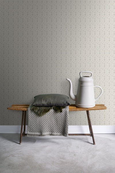 Dekorative Wand mit floral gemusterter Tapete, Holzbank, Kissen und Gießkanne.