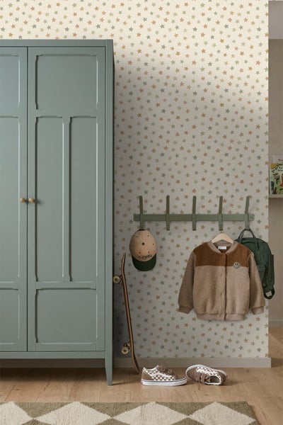 Organisiertes Kinderzimmer mit Sternentapete. Grüner Kleiderschrank aus Holz, Wandgarderobe mit Fleecejacke, Rucksack und Kappe sowie ein Skateboard.