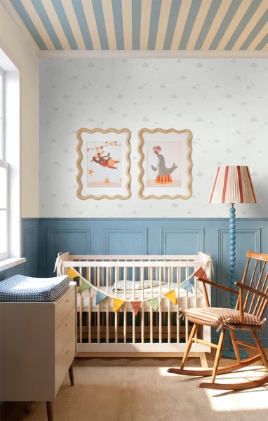 Kinderzimmer mit Holzbabybett, Wolkentapete, blauen Wandpaneelen, einem Schaukelstuhl und Zirkus-Wandbildern.