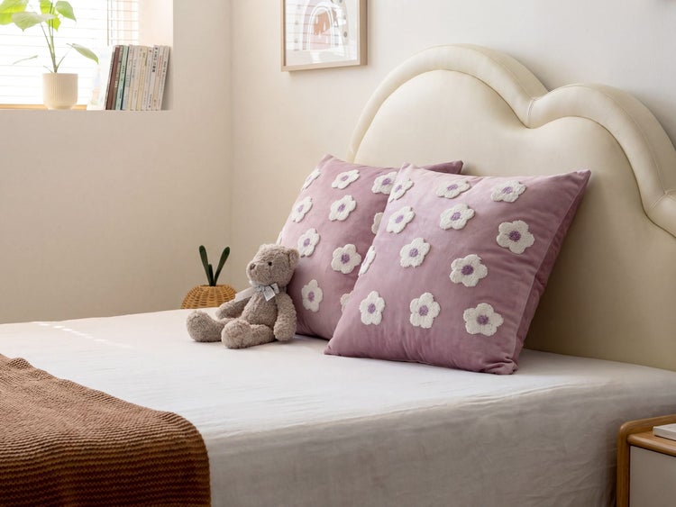 Zwei lila Zierkissen mit Blumenmuster auf einem hellen Bett mit gewelltem Kopfteil in einem hellen, organisierten Schlafzimmer.