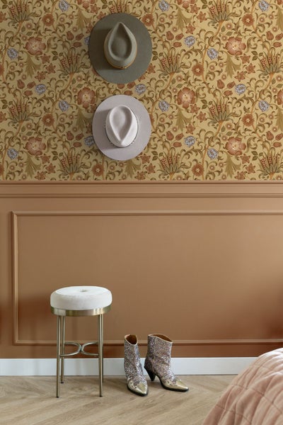 Wohnraum mit floral gemusterter Tapete, Wandpaneelen mit Zierleisten, einem Hocker und Stiefeln auf hellem Boden.