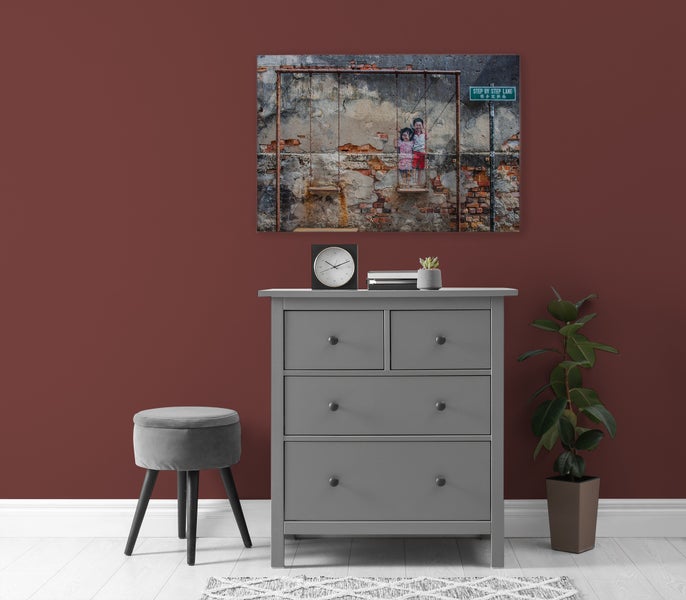 Wandbild mit Motiv Kinder auf einer Schaukel über einer grauen Kommode mit Hocker und Pflanze in einem modern eingerichteten Raum.