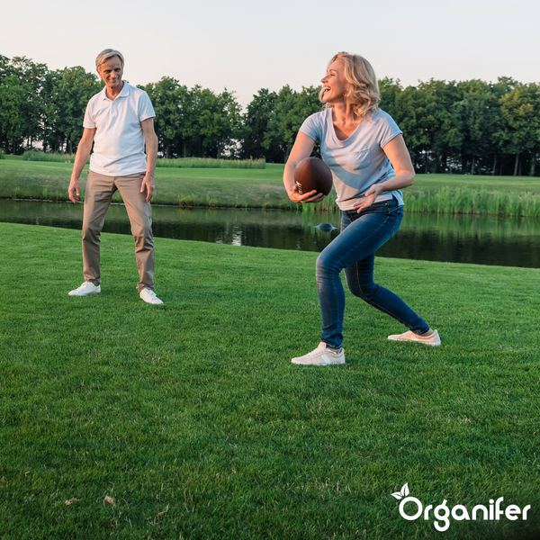 Ein Paar spielt American Football auf einem gepflegten grünen Rasen. Im Hintergrund befinden sich ein Teich und Bäume. Organifer Logo.