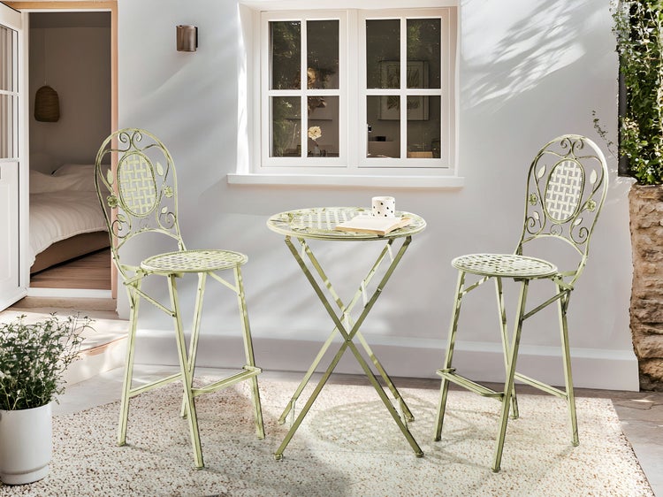 Szene mit Gartentisch und zwei Gartenstühlen auf einem Teppich im Freien vor einem Haus.