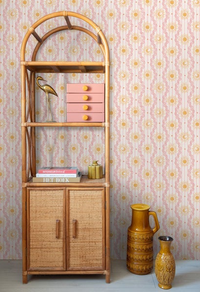 Vliestapete mit Sonnen- und Mondmuster sowie gewellten Streifen hinter einem Rattanregal und Keramikvasen.