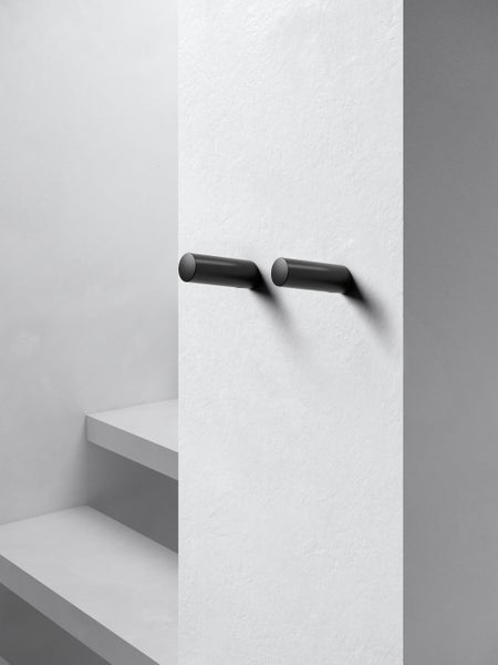 Zwei zylinderförmige Wandhaken in minimalistischem Design zur Wandmontage an einer weißen Wand.