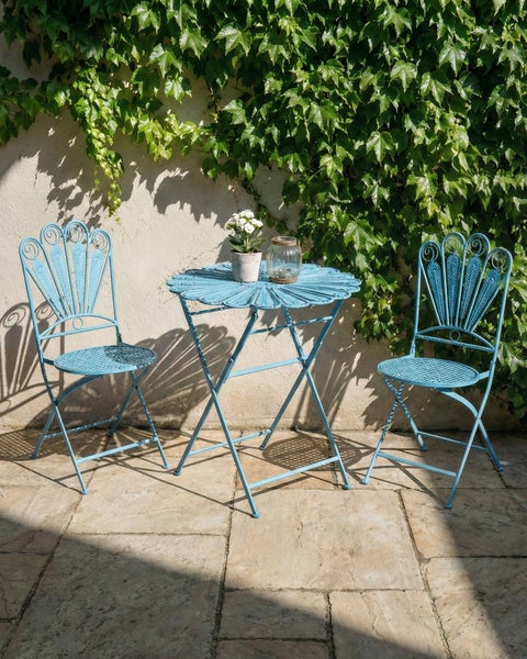 Gartenszene mit einem runden Tisch und zwei Stühlen aus Metall vor einer mit Efeu bewachsenen Wand