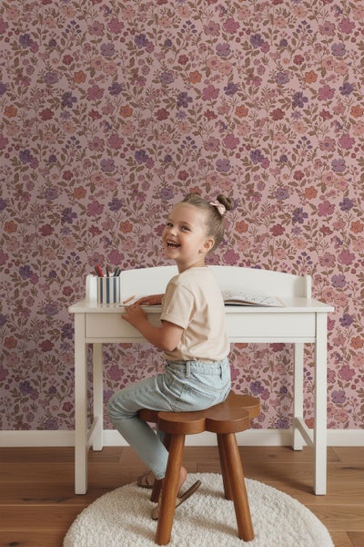 Kind sitzt an einem Schreibtisch vor einer floral gemusterten Tapete.