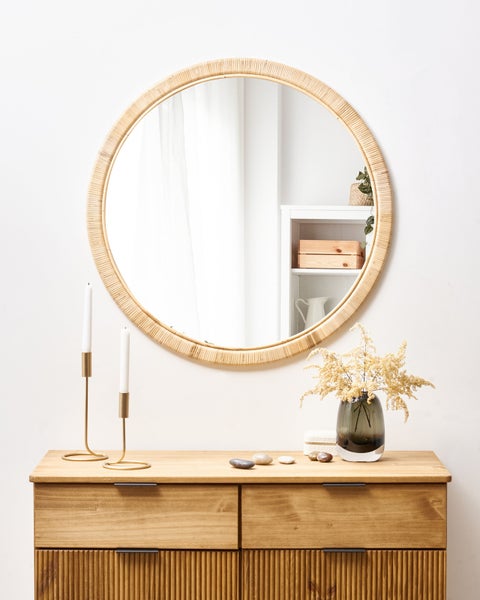 Dekoratives Interieur mit einem runden Spiegel über einer Holzkommode