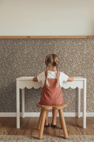 Mädchen sitzt an weißem Kinderschreibtisch mit Holzstuhl vor floraler Tapete