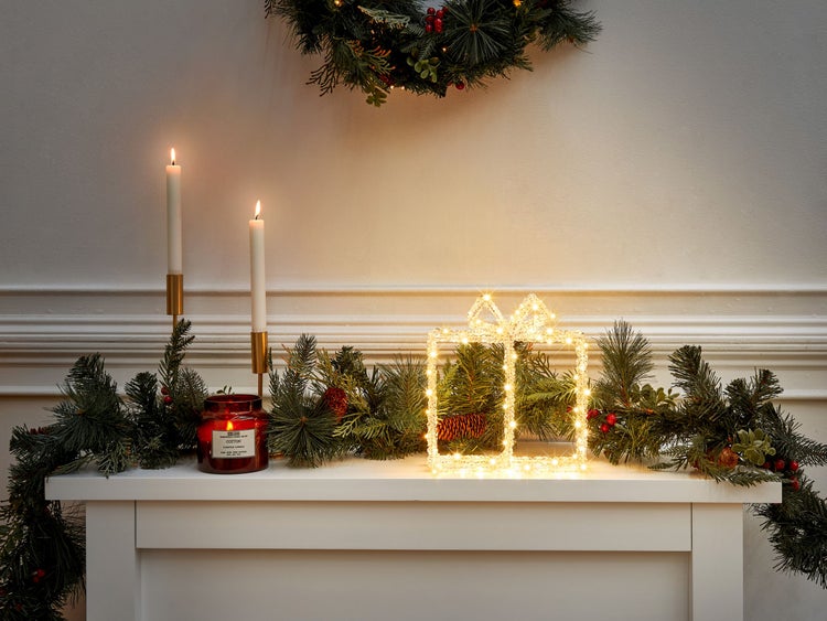 Festliche Dekoration mit LED Geschenk, Kerzen und Tannengirlande auf einem Kaminsims