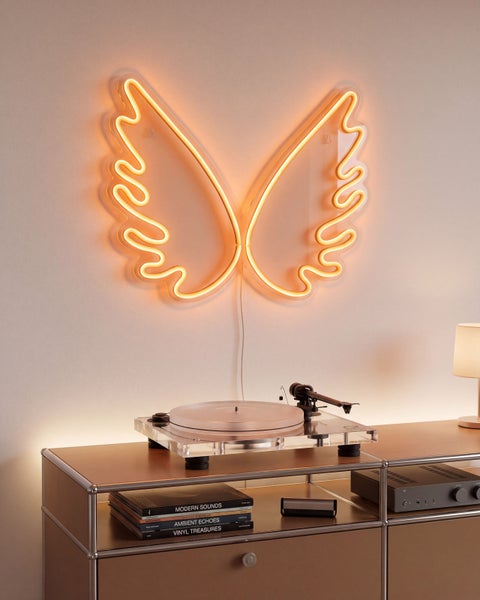 LED Neon Wandleuchte in Form von Engelsflügeln, montiert an einer hellen Wand über einem Plattenspieler auf einem Metallregal.
