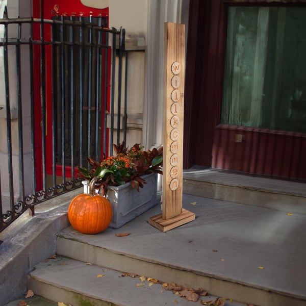 Dekorative Holztafel mit der Aufschrift Willkommen auf einer Treppe neben einem Kürbis und einem Blumenkasten.