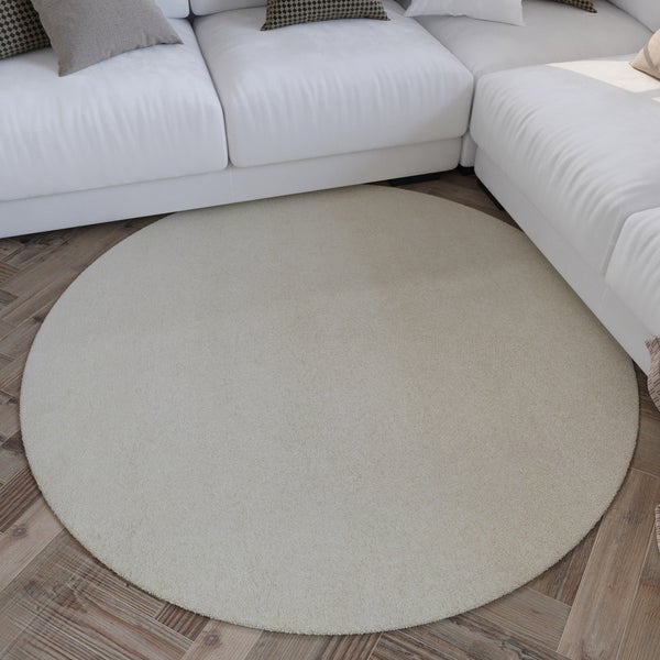 Runder Teppich auf Parkettboden in einem hellen Wohnzimmer mit weißem Sofa.