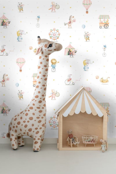 Kindertapete mit Zirkusmotiven wie Tieren, Heißluftballons und Riesenrädern im Kinderzimmer neben einer Plüschgiraffe und einem Holzspielhaus.