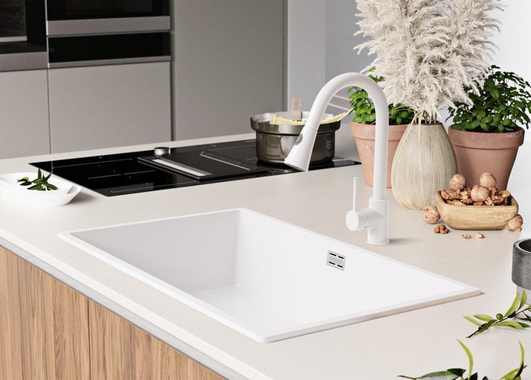 Küchenspüle mit Armatur auf einer Küchentheke, neben einem Kochfeld und verschiedenen dekorativen Elementen wie Pflanzen und einer Schale mit Nüssen.