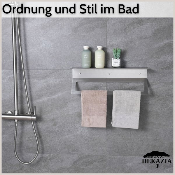 Duschablage und Badezimmerregal aus Edelstahl mit integriertem Handtuchhalter an einer Fliesenwand neben einer Duscharmatur. Dekazia Logo.