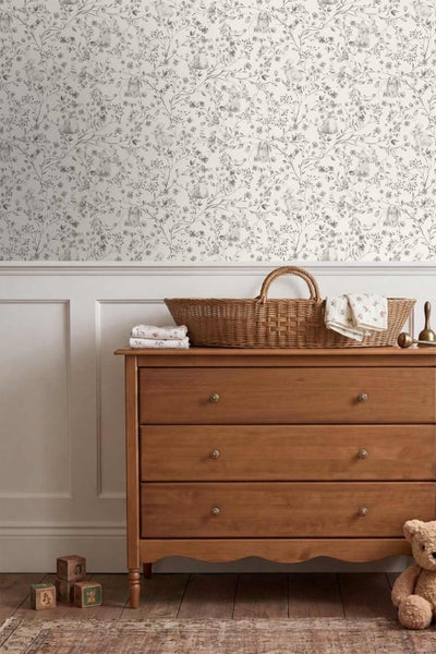 Tapete mit Hasen- und Blumenmuster im Kinderzimmer über einer Wandtäfelung und einer Holzkommode.