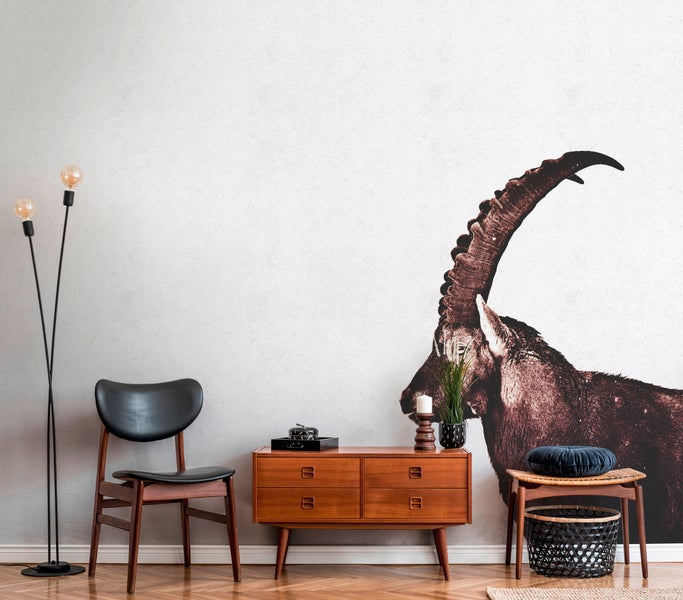 Heller Wohnraum mit Steinbock-Fototapete, modernem Sideboard aus Holz, Lederstuhl und Stehleuchte auf Parkettboden.