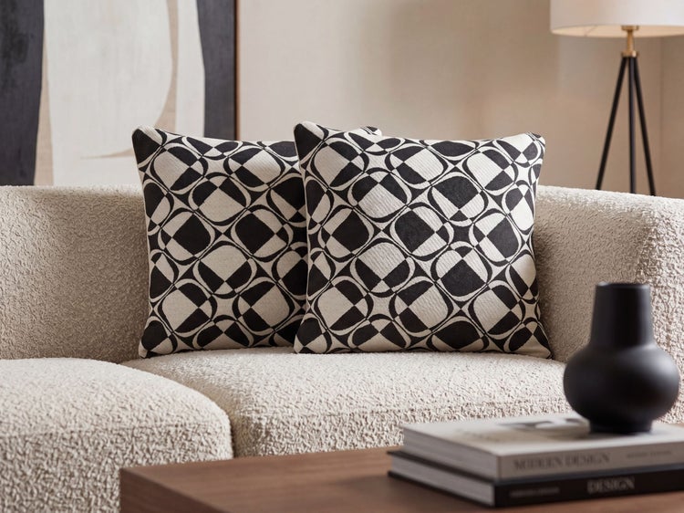 Zwei Dekokissen mit geometrischem Muster auf einem strukturierten Sofa in einem modern eingerichteten Wohnzimmer.