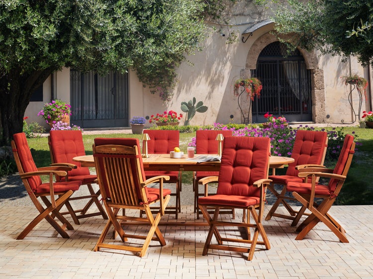 Gartenszene mit einem Holztisch und acht Holzstühlen mit Sitzkissen im Freien.