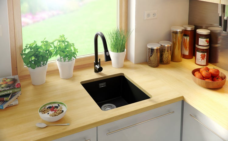 Küchenszene mit schwarzem Spülbecken, Armatur, Lebensmitteln und Pflanzen auf einer hellen Arbeitsplatte