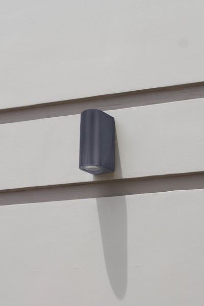 Zylindrische Wandleuchte aus Metall wirft Licht auf eine Backsteinmauer.