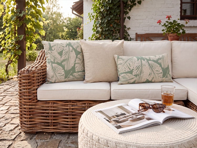 Gartenlounge aus Rattan mit weichen Polstern und dekorativen Kissen im Pflanzenmuster auf einer Terrasse.