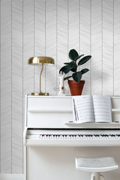 Szene mit einer weißen Tapete mit Pfeilmuster, einem Klavier, einer Lampe und einer Zimmerpflanze.