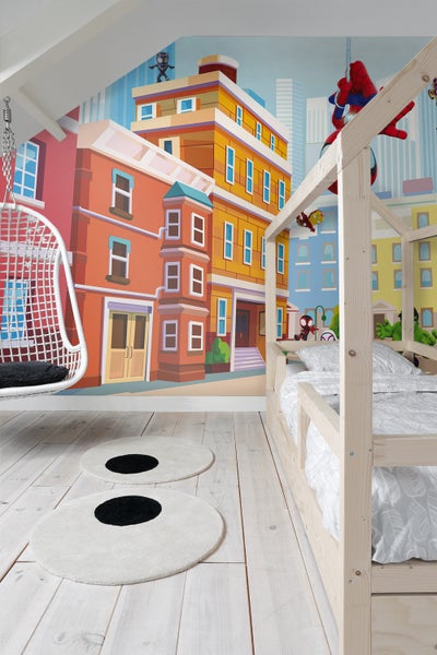 Helles Kinderzimmer mit einem Holzhausbett, einer Hängeschaukel und runden Teppichen vor einer Wandtapete mit Stadtmotiv.