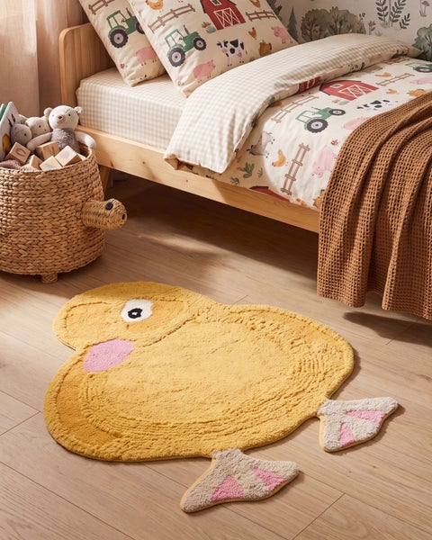 Kinderzimmer mit Holzbett, Bauernhofbettwäsche, Korb mit Stofftieren und einem flauschigen Enten-Teppich auf dem Boden.