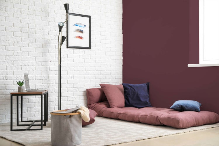 Modernes Zimmer mit dunkelroter Wand, weißer Ziegelwand, flachem Futon Sofa, Stehlampe und kleinem Beistelltisch auf hellem Teppich.